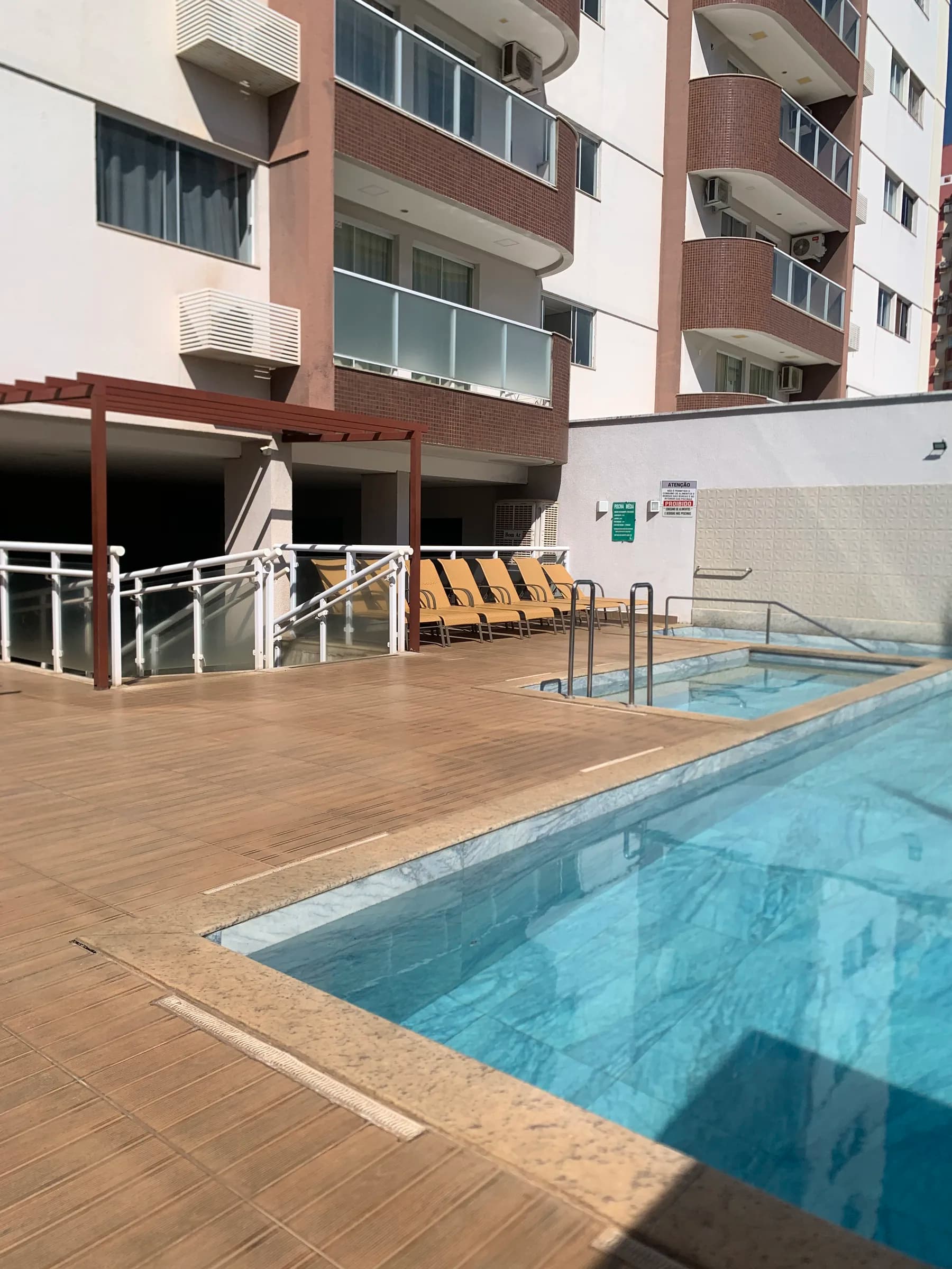 Deck, espreguiçadeiras e o prédio visto da piscina